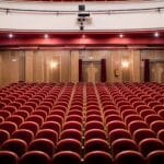 Pusta sala teatralna z czerwonymi fotelami i drewnianymi ś